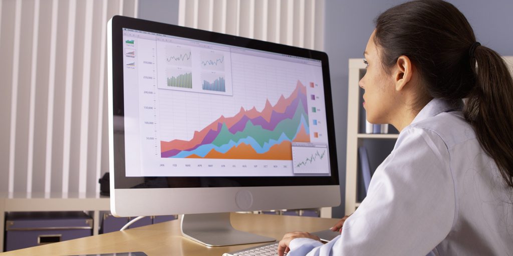 Women sitting and looking at computer monitor screen, on screen is a spreadsheet with a chart
