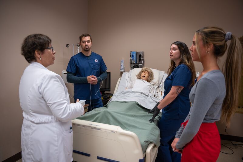 Associate degree in nursing, lab, instructor with students surrounding simulator asking questions