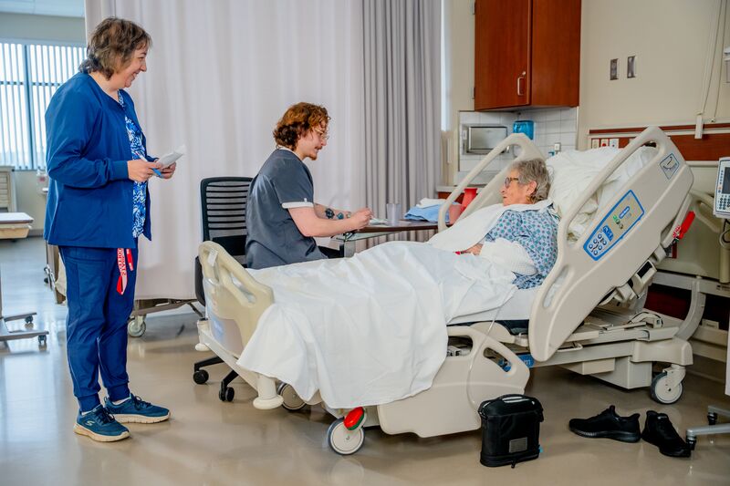 certified nurse aide (CNA), lab, student, instructor and patient in bed talking