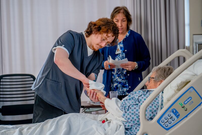 certified nurse aide (CNA), lab, student, instructor and patient in bed cleaning hand