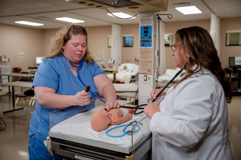 RN completion for LPN, female student working on infant nursing simulator with instructor