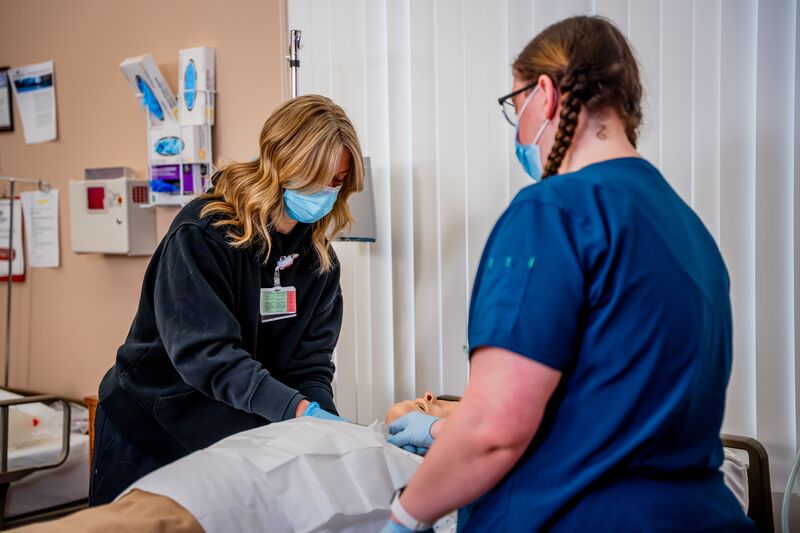 RN completion for LPN, two female students work on nursing simulator in lab