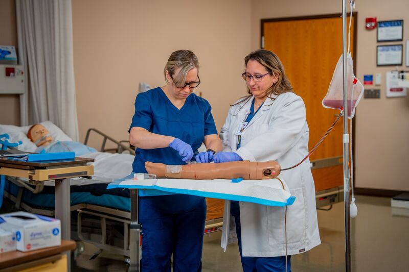 RN completion for LPN, female student and instructor add IV to simulation arm