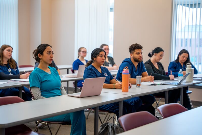RN completion for LPN, students in traditional classroom with laptops and textbooks listening to instructor lecture