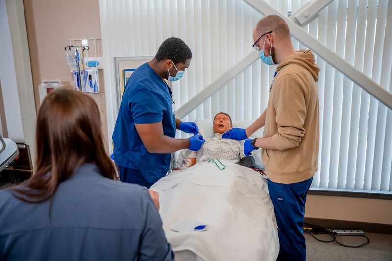 RN completion or paramedic, paramedic to RN lab, two students working on simulator as instructor watches