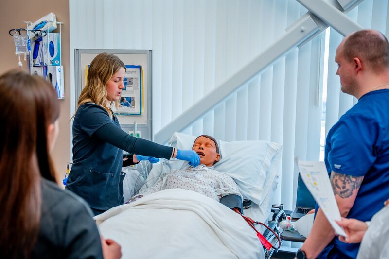 RN completion or paramedic, paramedic to RN lab, two students working on simulator as instructor watches