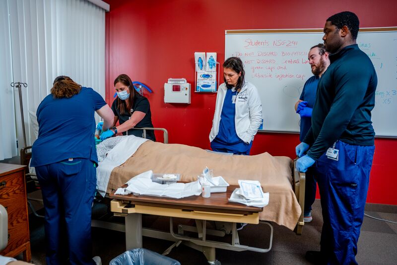 RN completion or paramedic, paramedic to RN lab, instructors with students surrounding bed and simulator learning
