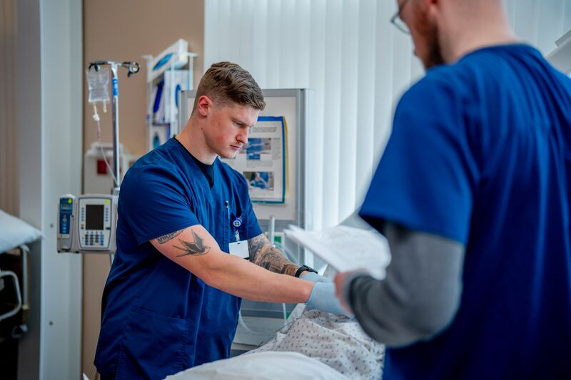RN completion or paramedic, paramedic to RN lab, two male students working on simulator