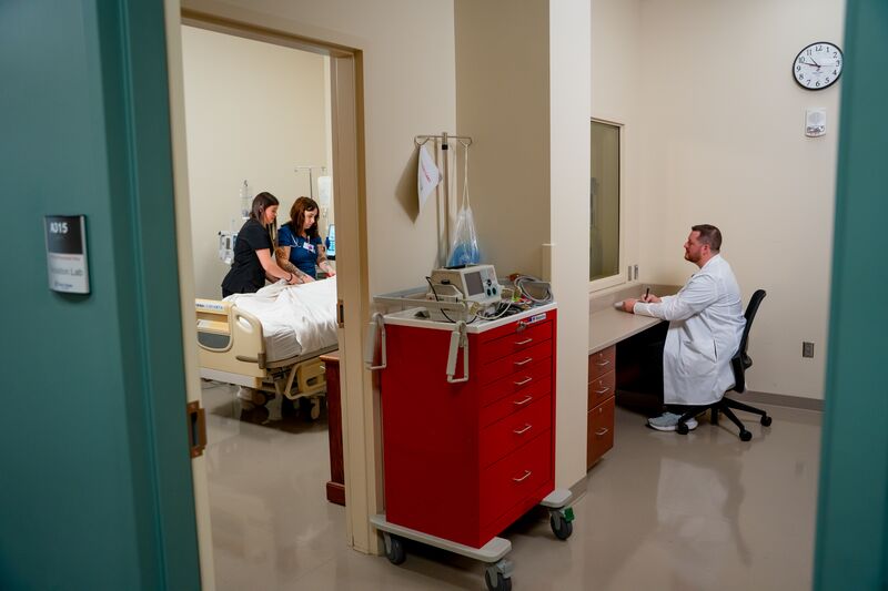 Practical Nursing, LPN, instructor watching students in lab through a two-way mirror, students seen through the doorway