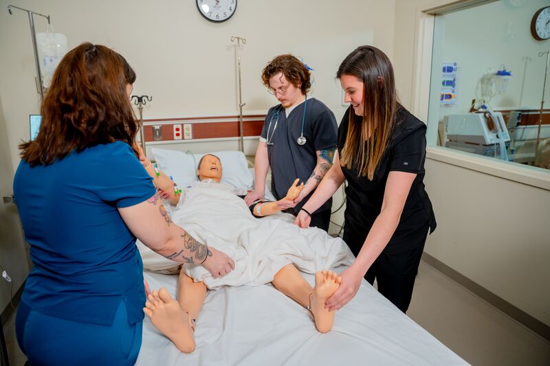 Practical Nursing, LPN, two female students and one male student working on nursing simulator at bedside