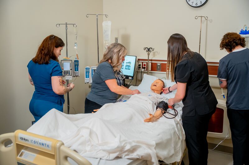 Practical Nursing, LPN, three female students and one male student working on nursing simulator with instructor watching