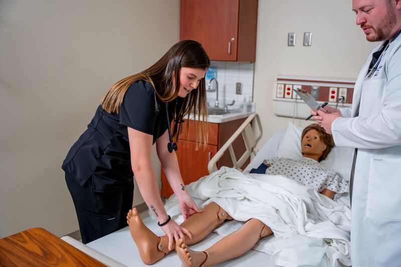 Practical Nursing, LPN, female student checking leg of nursing simulator with instructor watching