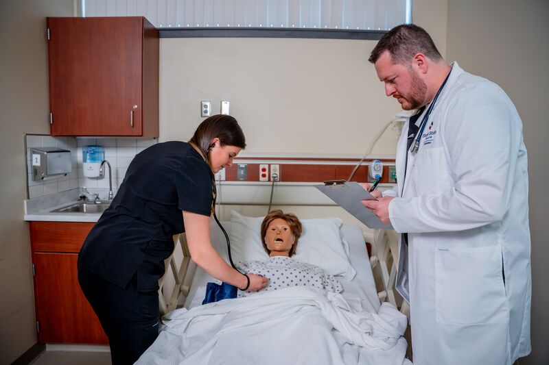 Practical Nursing, LPN, female student working with nursing simulator at bedside with instructor watching