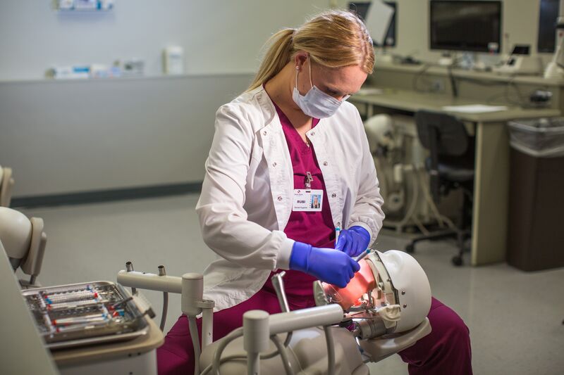 Female dental hygiene student in white lab coat working on simulator