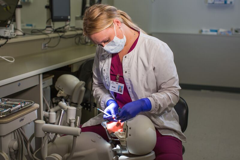 Female dental hygiene student in white lab coat working on simulator