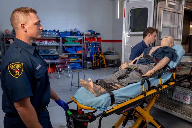 Two male EMS students placing simulator on gurney in the back of an ambulance
