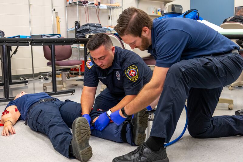 Two EMS students securing leg of female student, demonstration in classroom