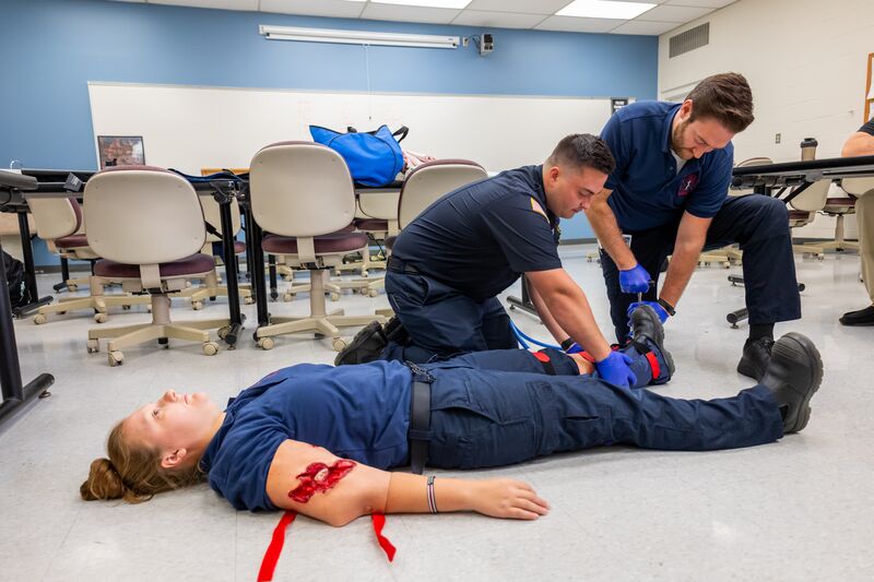 Two EMS students securing leg of female student, demonstration in classroom