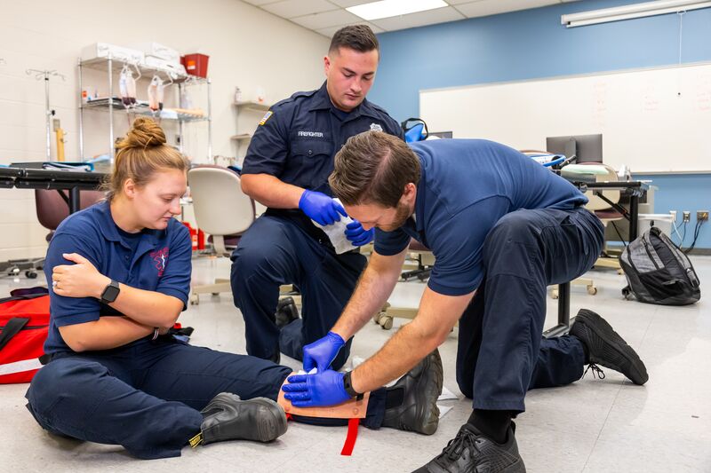 Two EMS students securing leg of female student, demonstration in classroom
