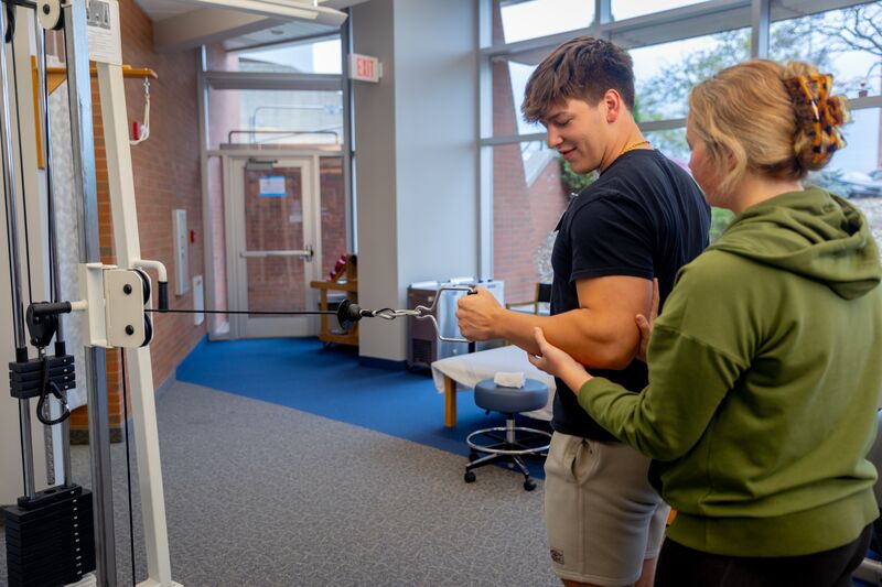 Physical therapy assisting program, female student helping male student with arm exercise