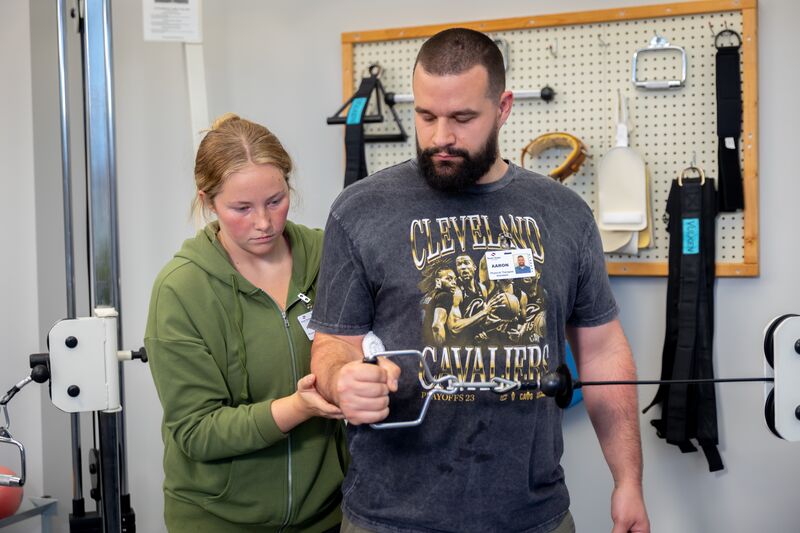 Physical therapy assisting program, one female student working with male student on arm exercise