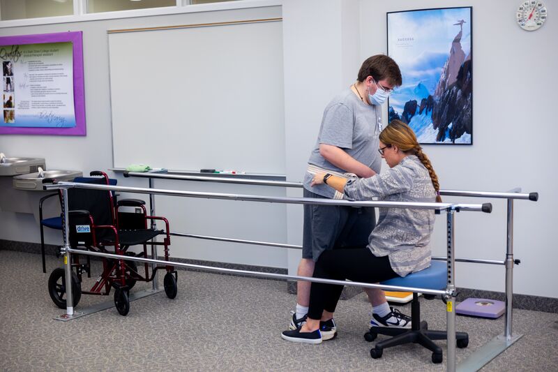 Physical therapy assisting program, female student helping male student to walk