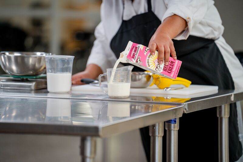 hands from culinary student pouring cream into measure glass