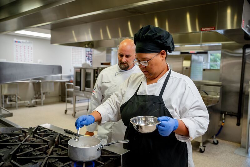 Female culinary student stirring pot while instructor oversees