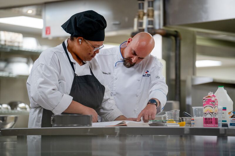 Culinary arts student and instructor looking through cookbook