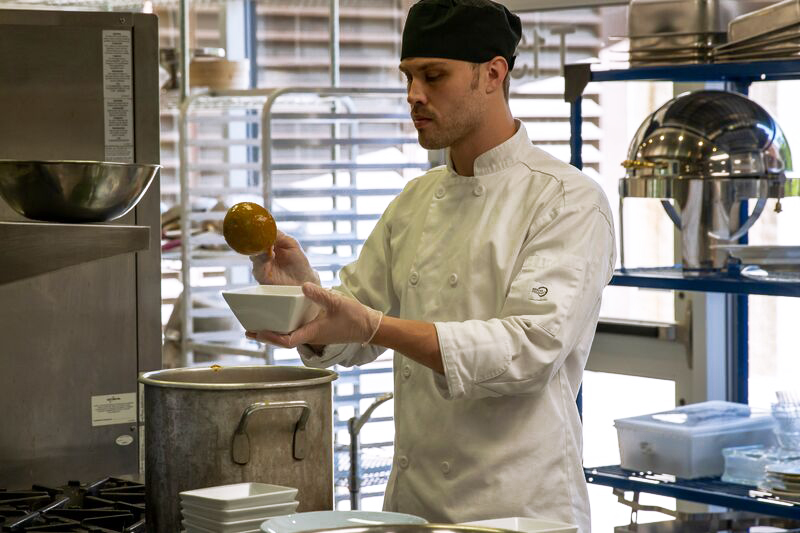 male culinary student scooping sauce into a dish