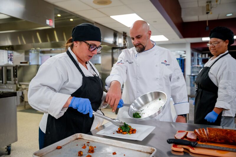 Culinary arts instructor working with female student to prepare a dish