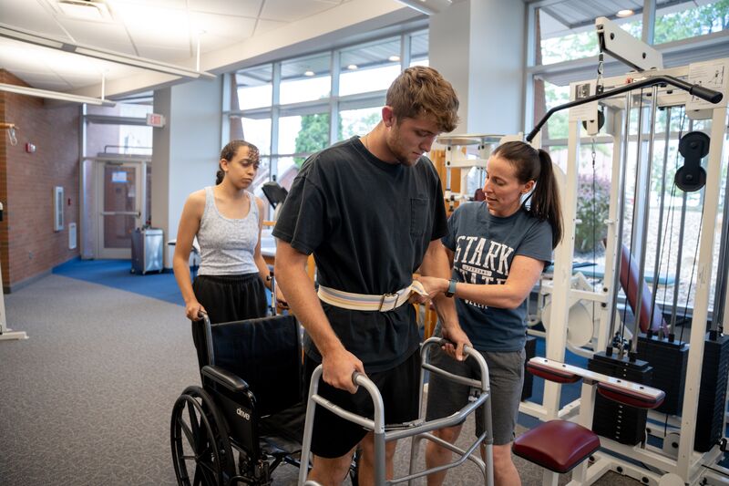 Physical therapy assisting program, two female students helping male student to walk with walker