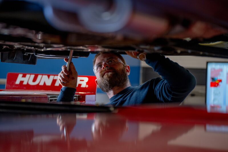 Male automotive student wearing protective eyewear working under a car with wrench