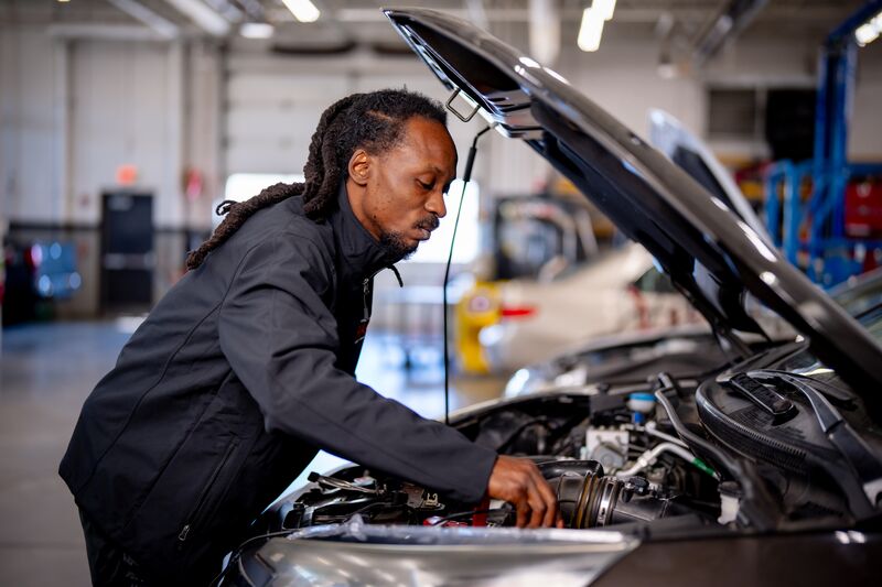 male student working under hood of car