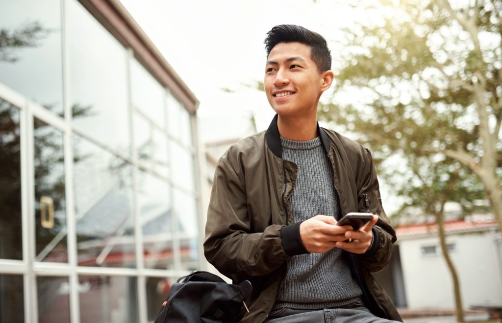 International students, Campus, education and student using phone for social media post update on study ideas, tips or scholarship application. College or university asian man on smartphone for online course information faq