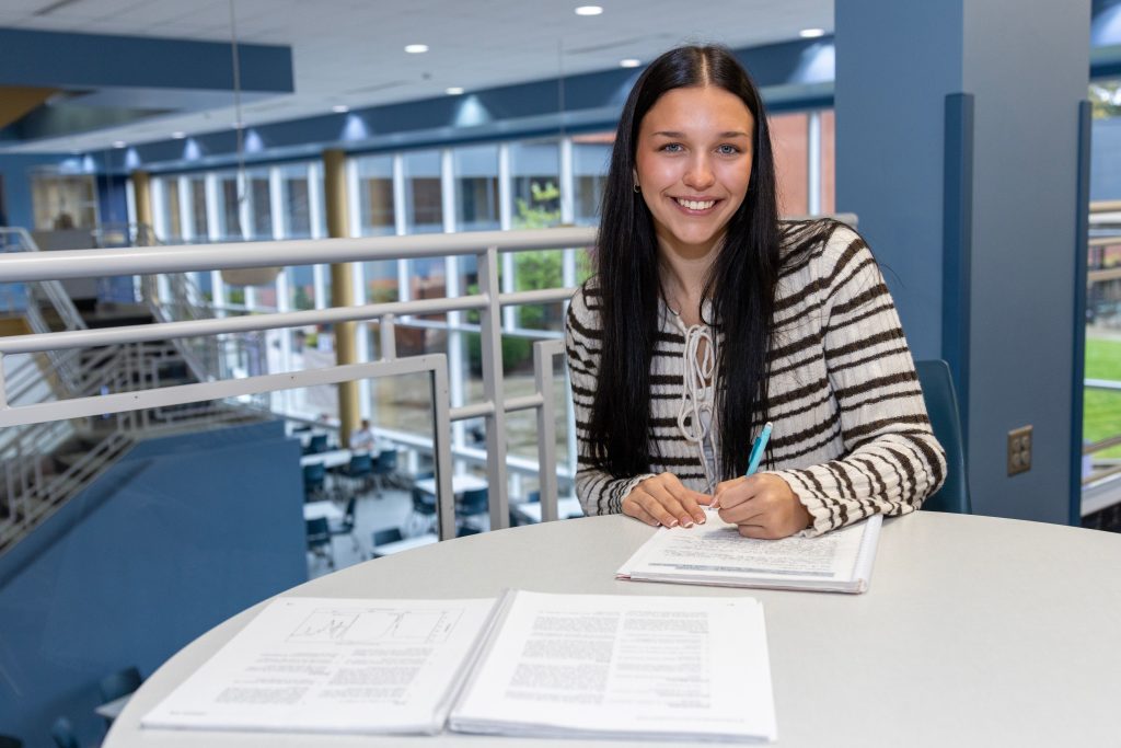 Transfer students, female student smiling at a table with notebook and homework