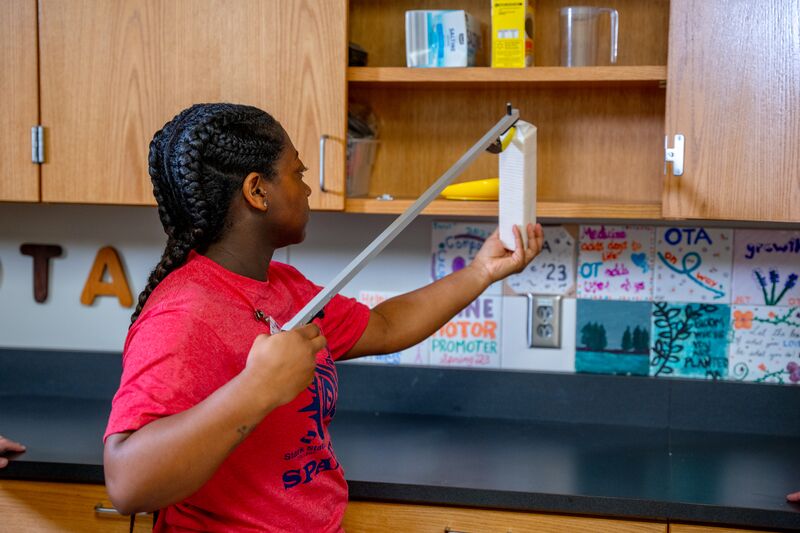 Occupational therapy, student using grabber to get object out of cupboard