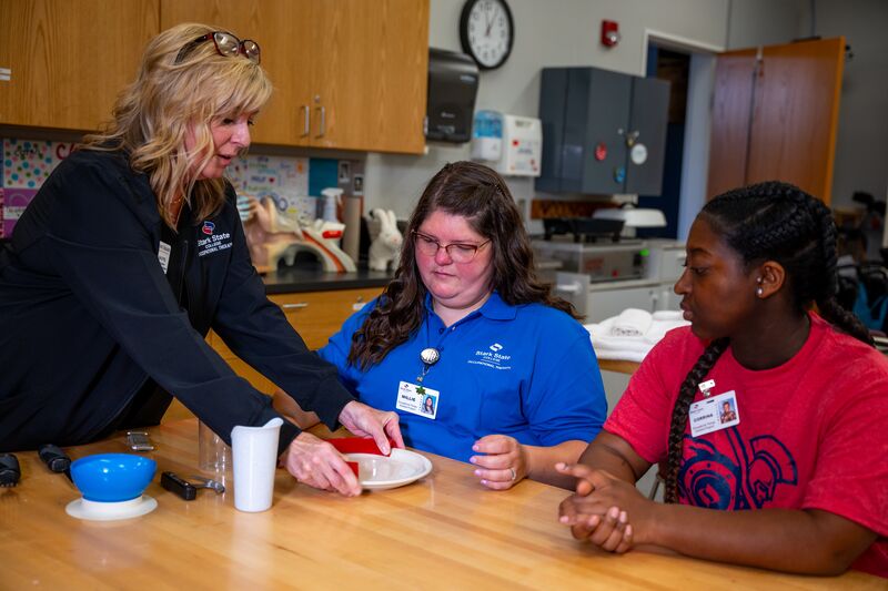 Occupational therapy, instructor working with two students on lifting plates at that table