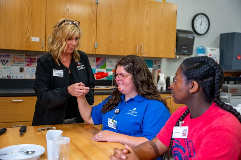 Occupational therapy, two female students and instructor working on spoon feeding