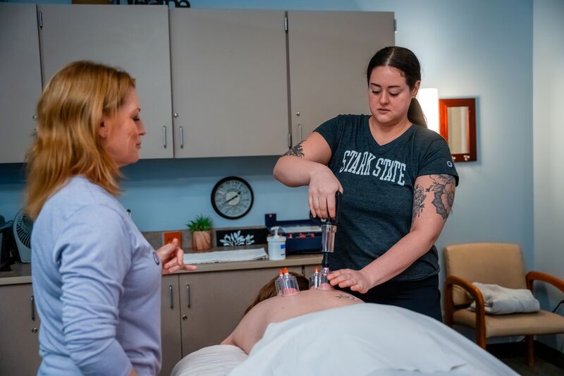 Female massage therapy student receiving instruction from female instructor while applying cupping technique to patient's back