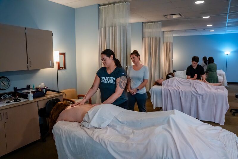 Female massage therapy student receiving instruction from female instructor while massage patient's back