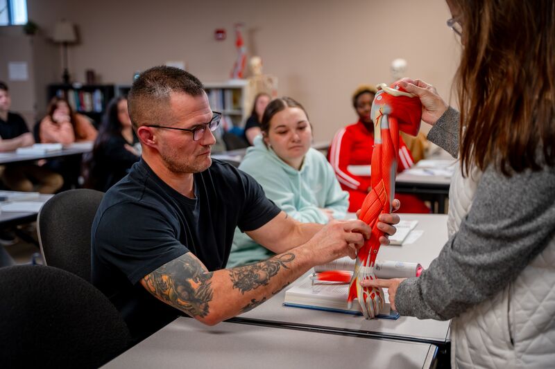 Massage therapy, male student working with muscles on simulation arm while instructor holds the simulator