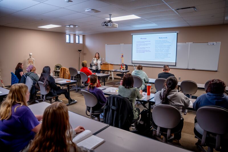 Massage therapy classroom, students sitting at tables with instructor at front of class