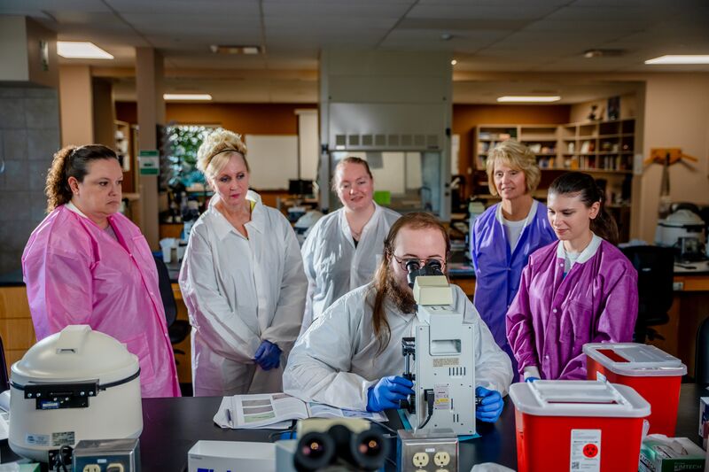 Medical laboratory, male student looking through microscope as other students and instructor watch