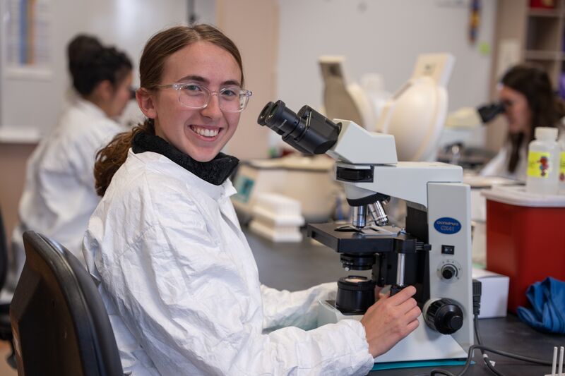 Medical laboratory, female student smiling at microscope
